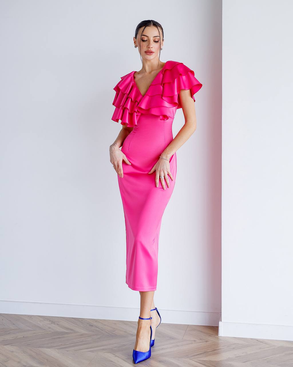 Woman wearing a bright pink dress with ruffled sleeves against a white wall.