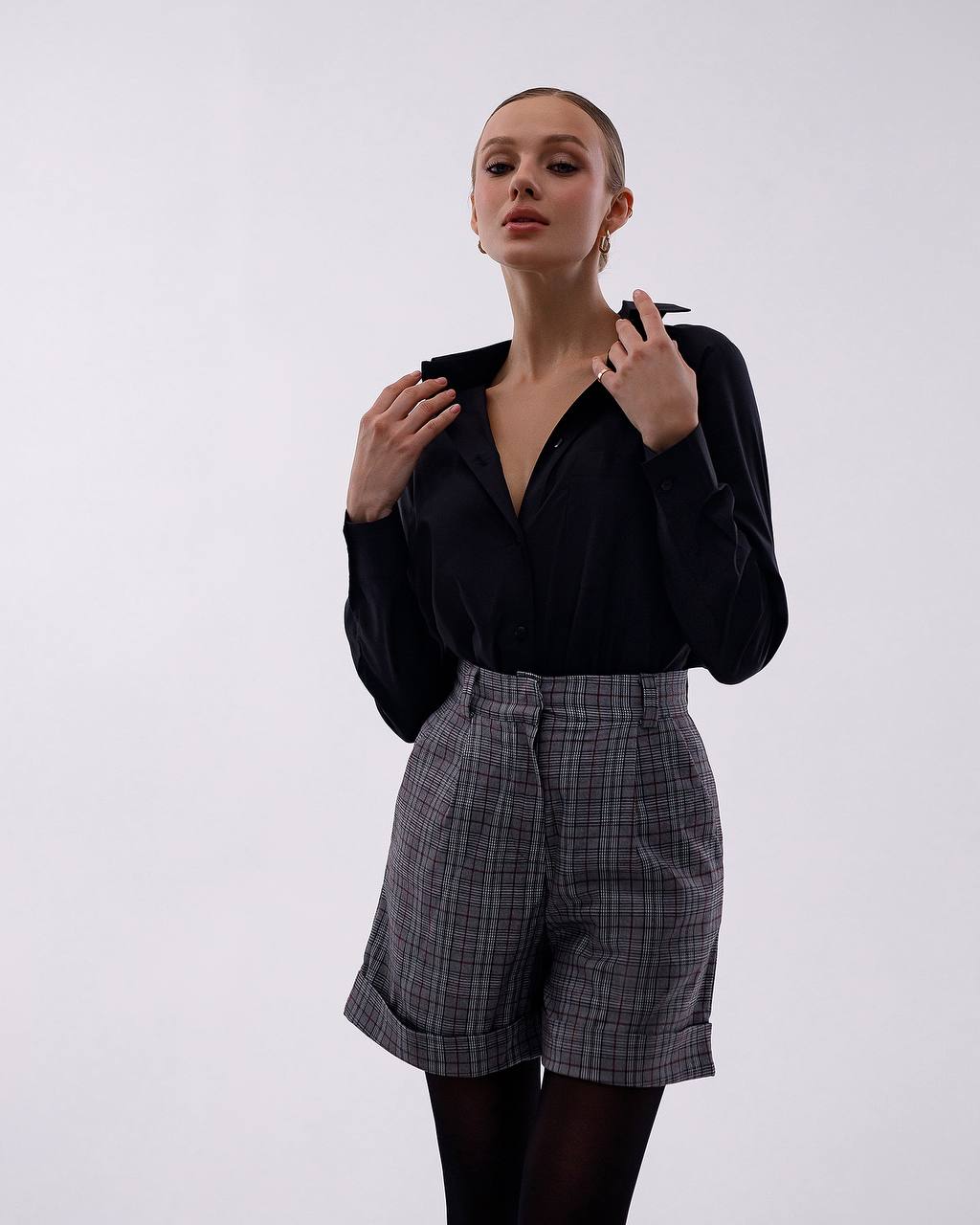 Woman wearing a black blouse and plaid shorts against a white background