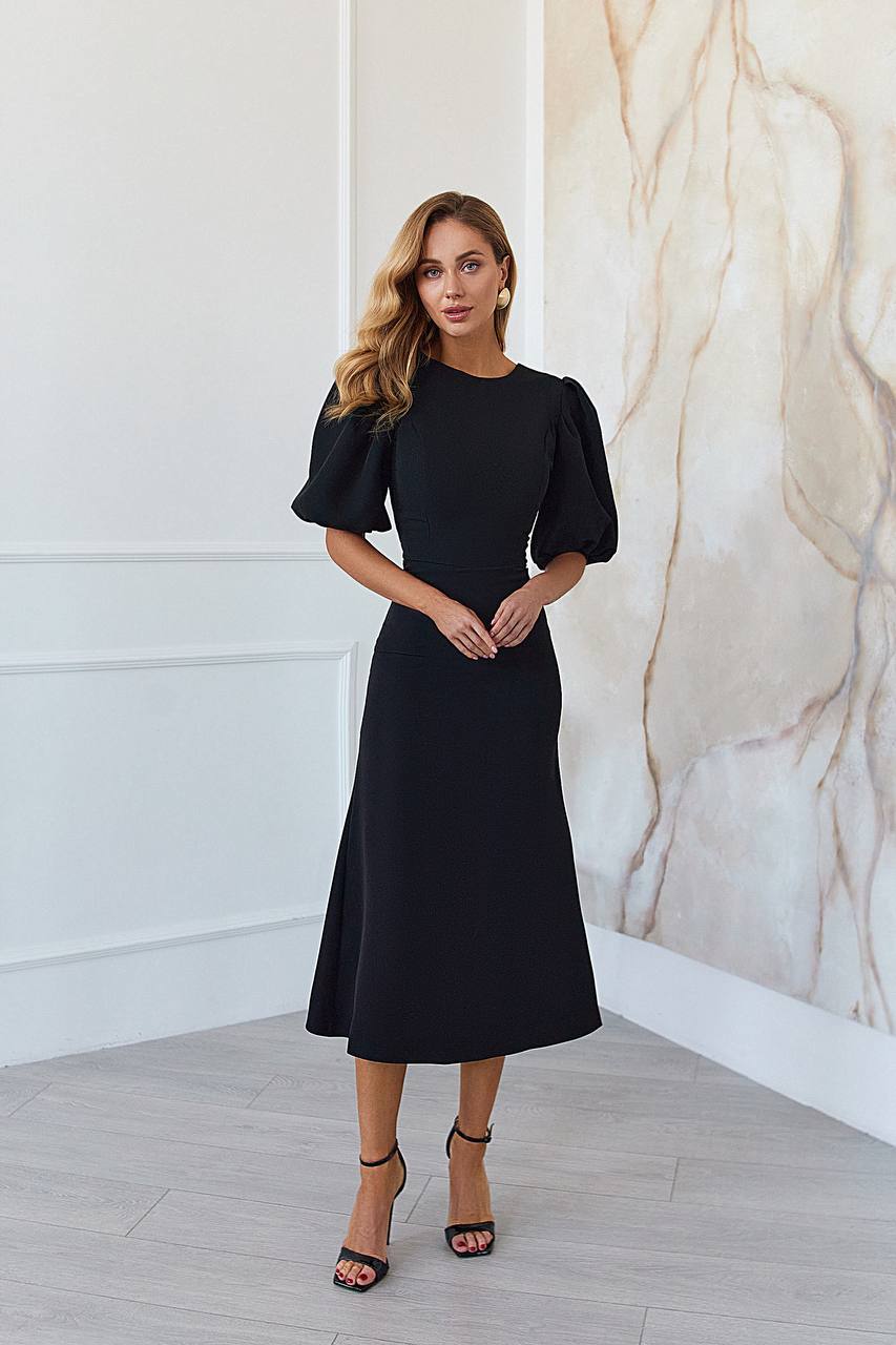 Woman wearing a black dress standing against a marble wall.