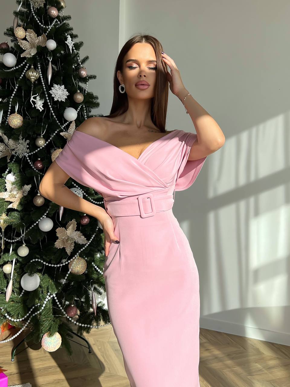 Woman in a pink dress standing next to a decorated Christmas tree indoors.