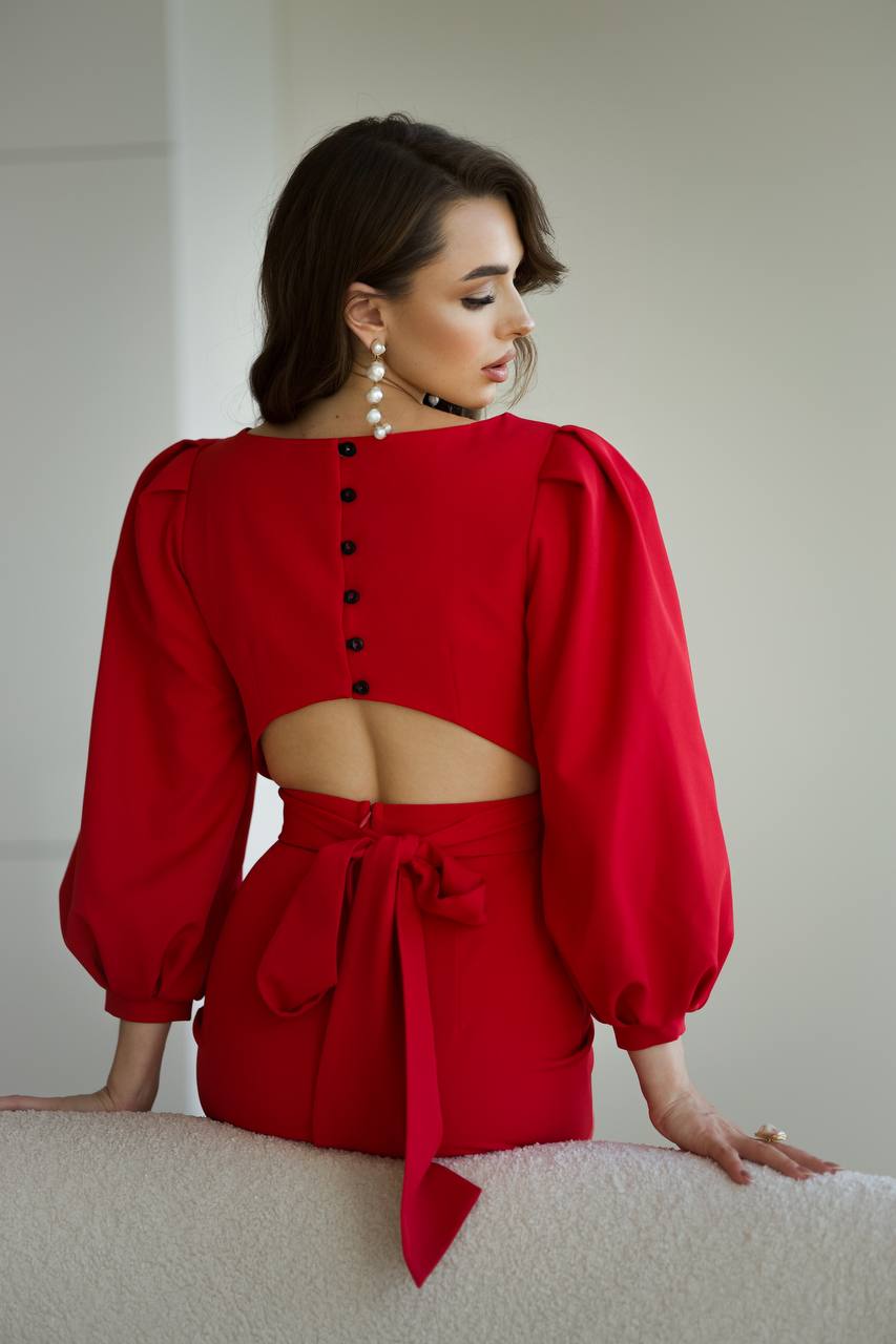 Woman wearing a red dress with cut-out design and puff sleeves against a plain background
