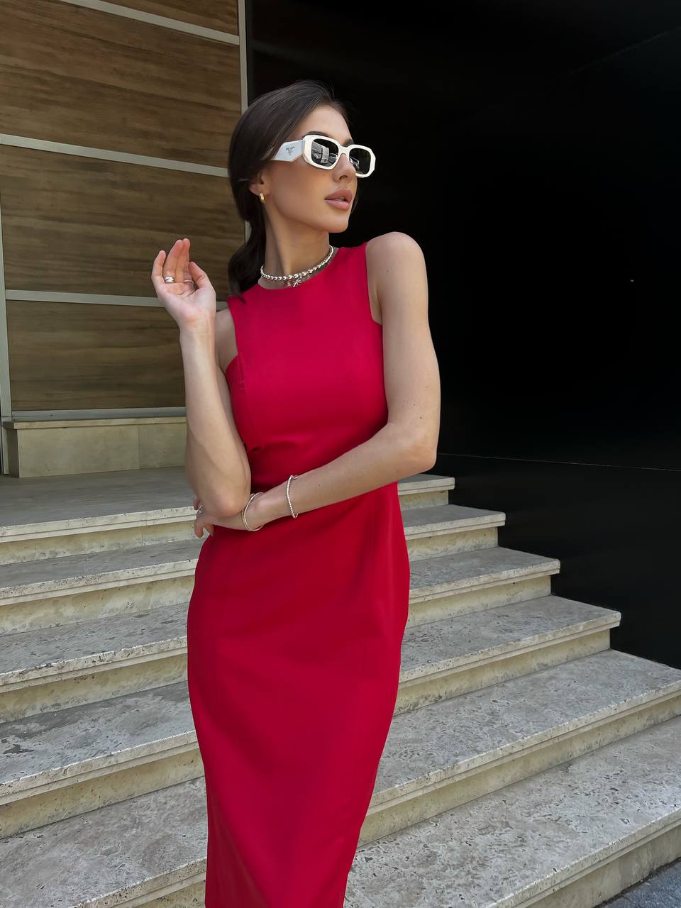 Woman in a red dress standing on steps wearing sunglasses.
