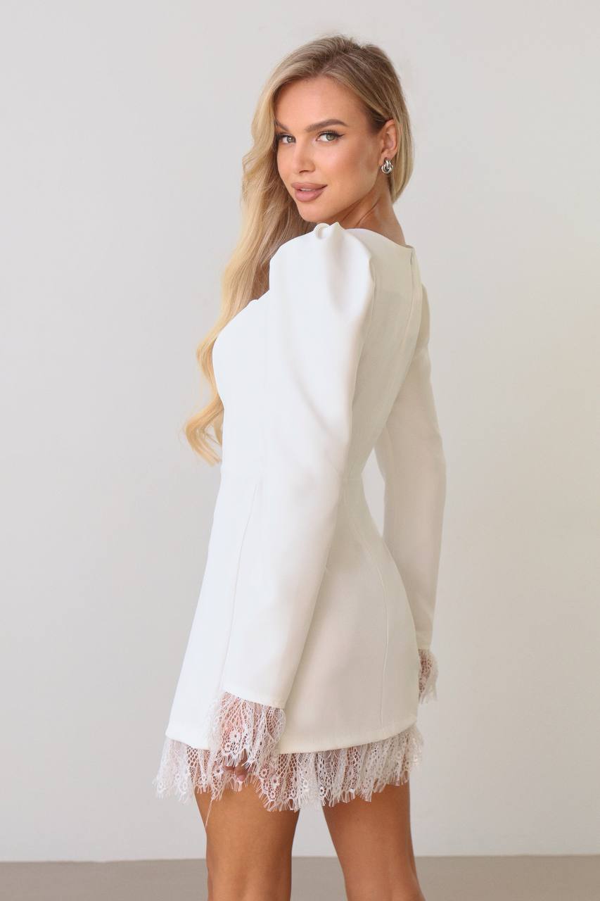 Woman wearing a white dress with lace hem against a plain background