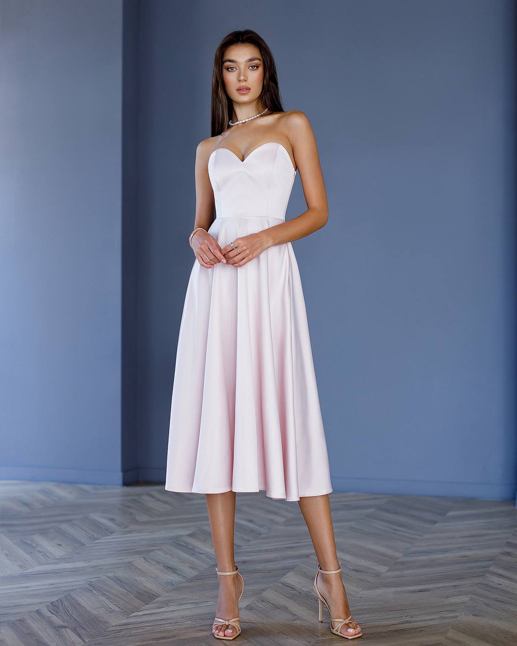 Woman wearing a white strapless dress against a blue wall.