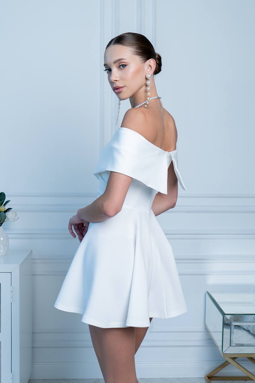 Woman wearing a white off-shoulder dress in a minimalistic room.