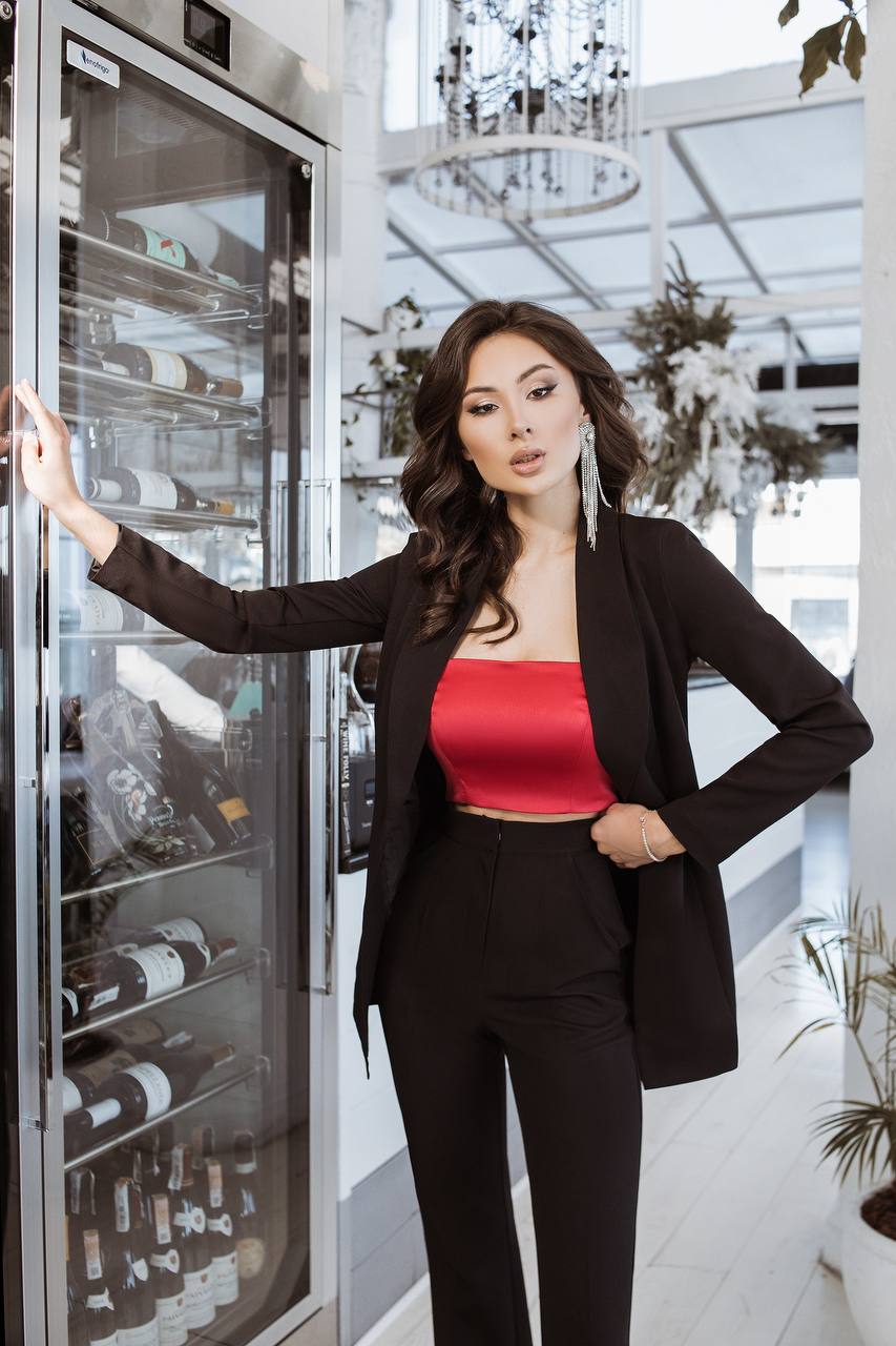 Woman in a black blazer and red top standing next to a wine refrigerator.