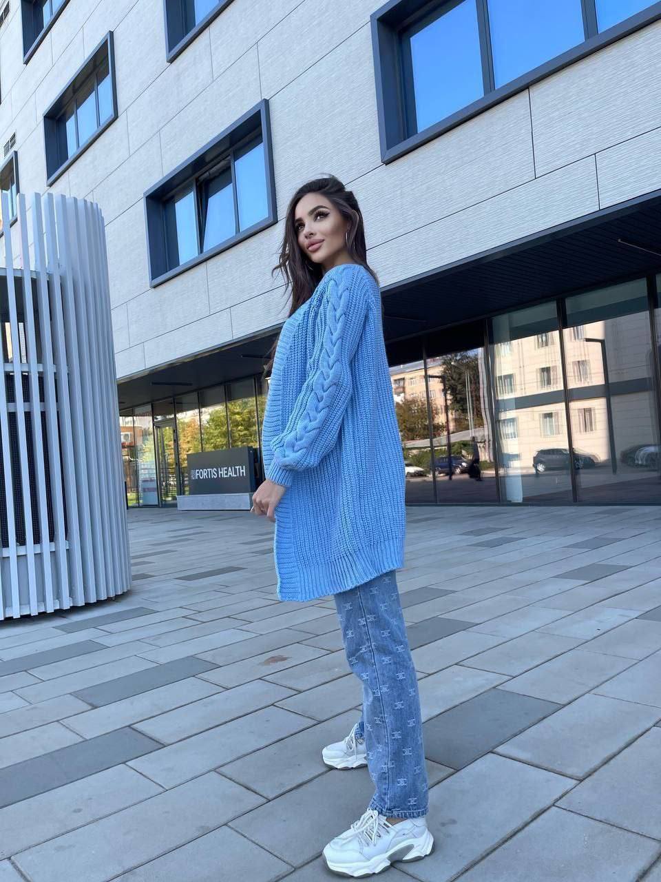 Woman wearing a blue sweater and jeans standing on a sidewalk in front of a building.