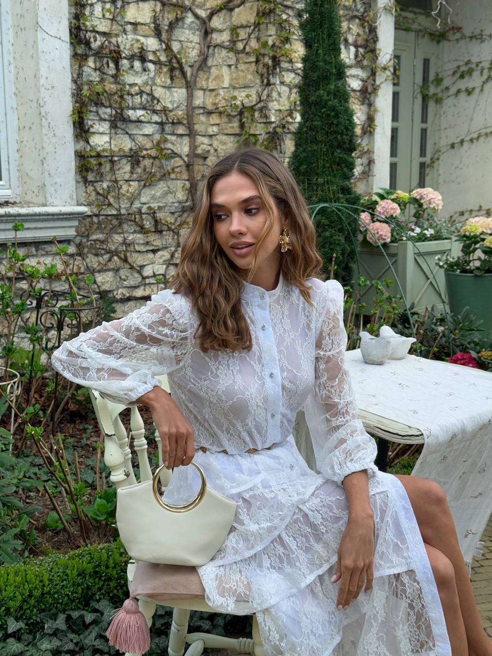 Woman in a white lace dress sitting outdoors with a garden background
