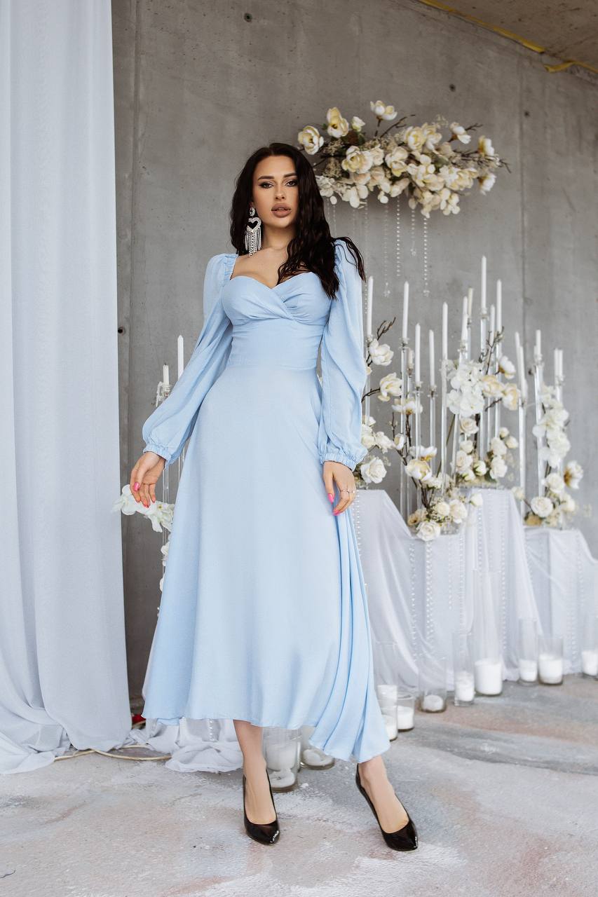 Woman in a light blue dress standing in front of a decorative floral arrangement and candles.
