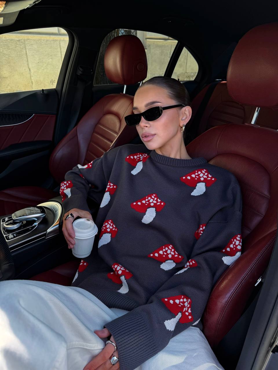Person wearing a sweater with red mushroom patterns sitting inside a car.