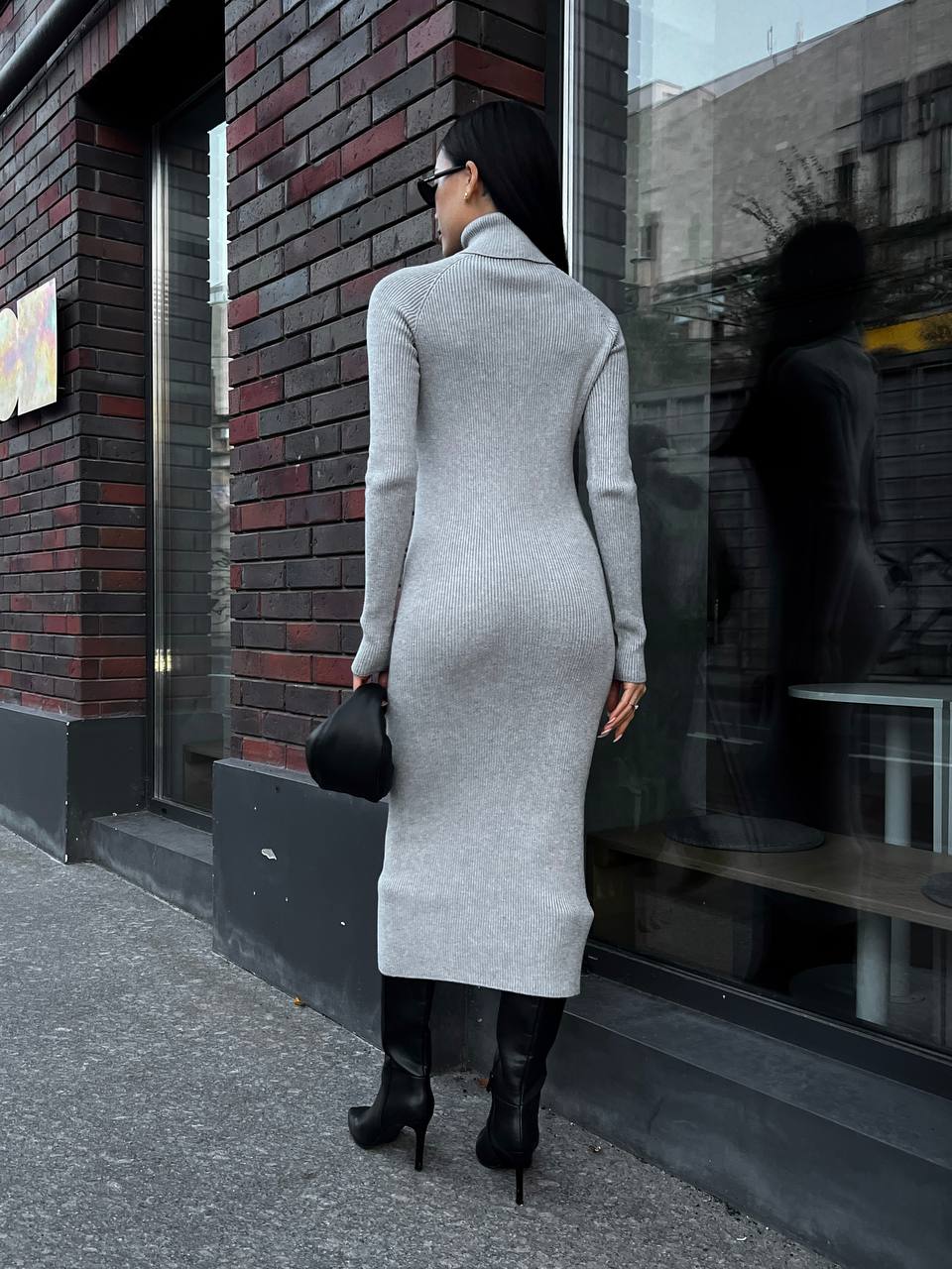 Woman in a long gray dress standing on a sidewalk next to a brick building.