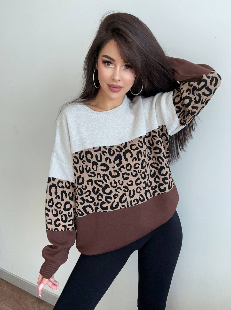 Woman wearing a sweater with a leopard print pattern against a plain background