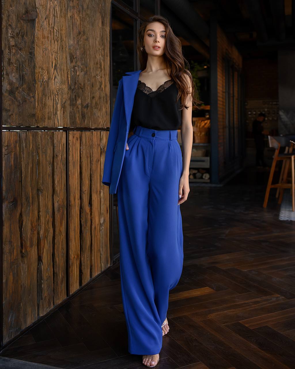 Woman wearing a blue outfit standing against a wooden wall.
