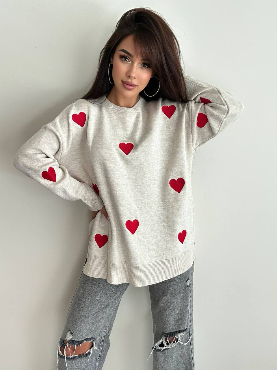 Woman wearing a beige sweater with red heart patterns against a plain background