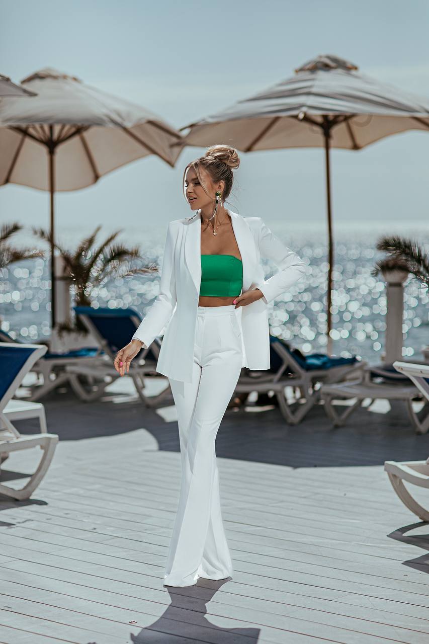 Woman in a white suit with a green top standing on a deck with umbrellas and lounge chairs.
