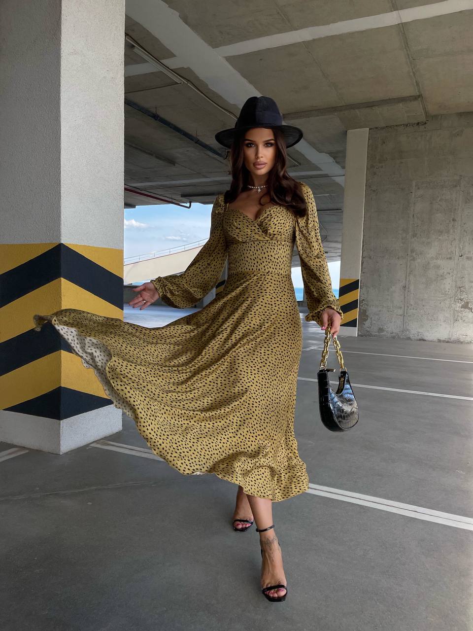 Woman in a yellow dress and black hat walking in an urban setting.
