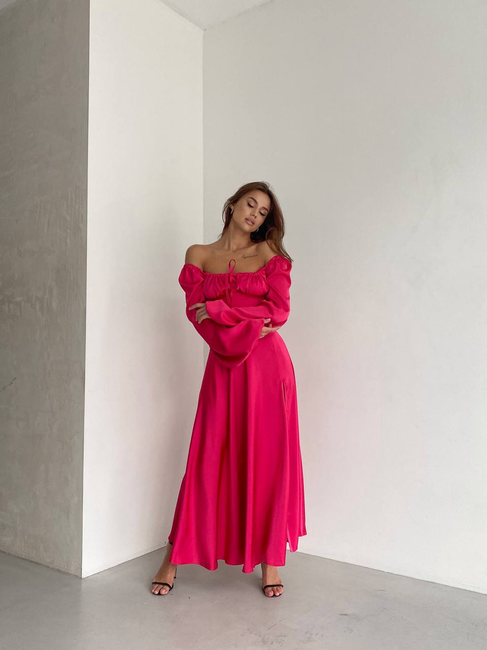 Woman in a bright pink off-shoulder dress standing against a white wall.
