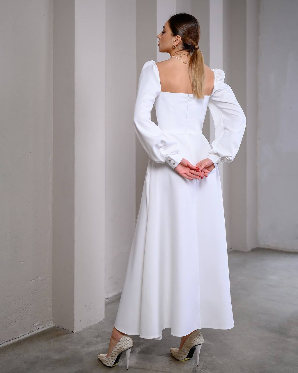 Woman wearing a white dress with long sleeves in a minimalistic setting