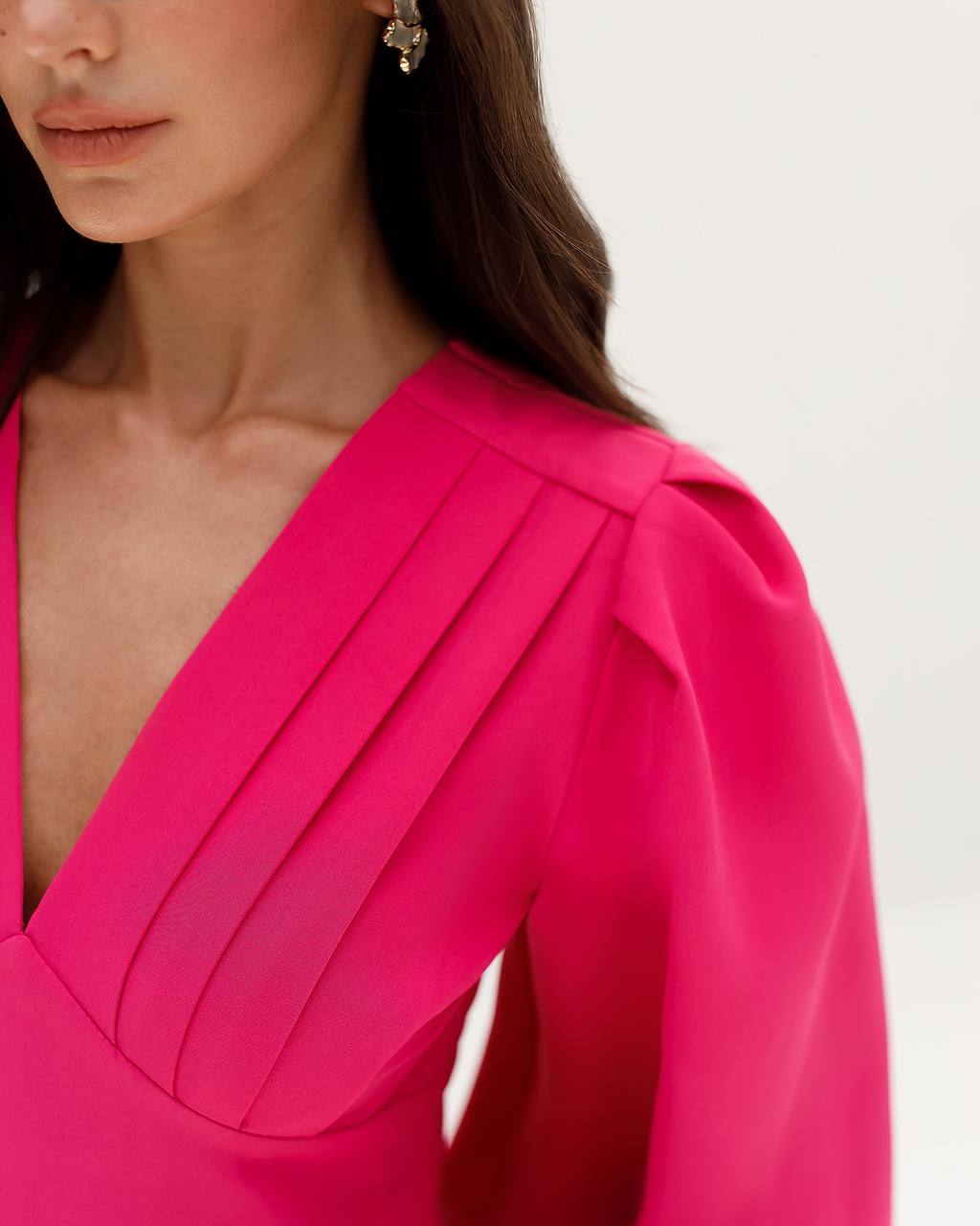Close-up of a bright pink dress with a V-neck and bow detail on a white background