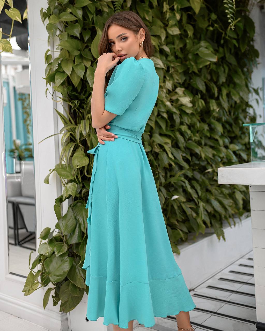 Woman in a turquoise dress standing against a green leafy background