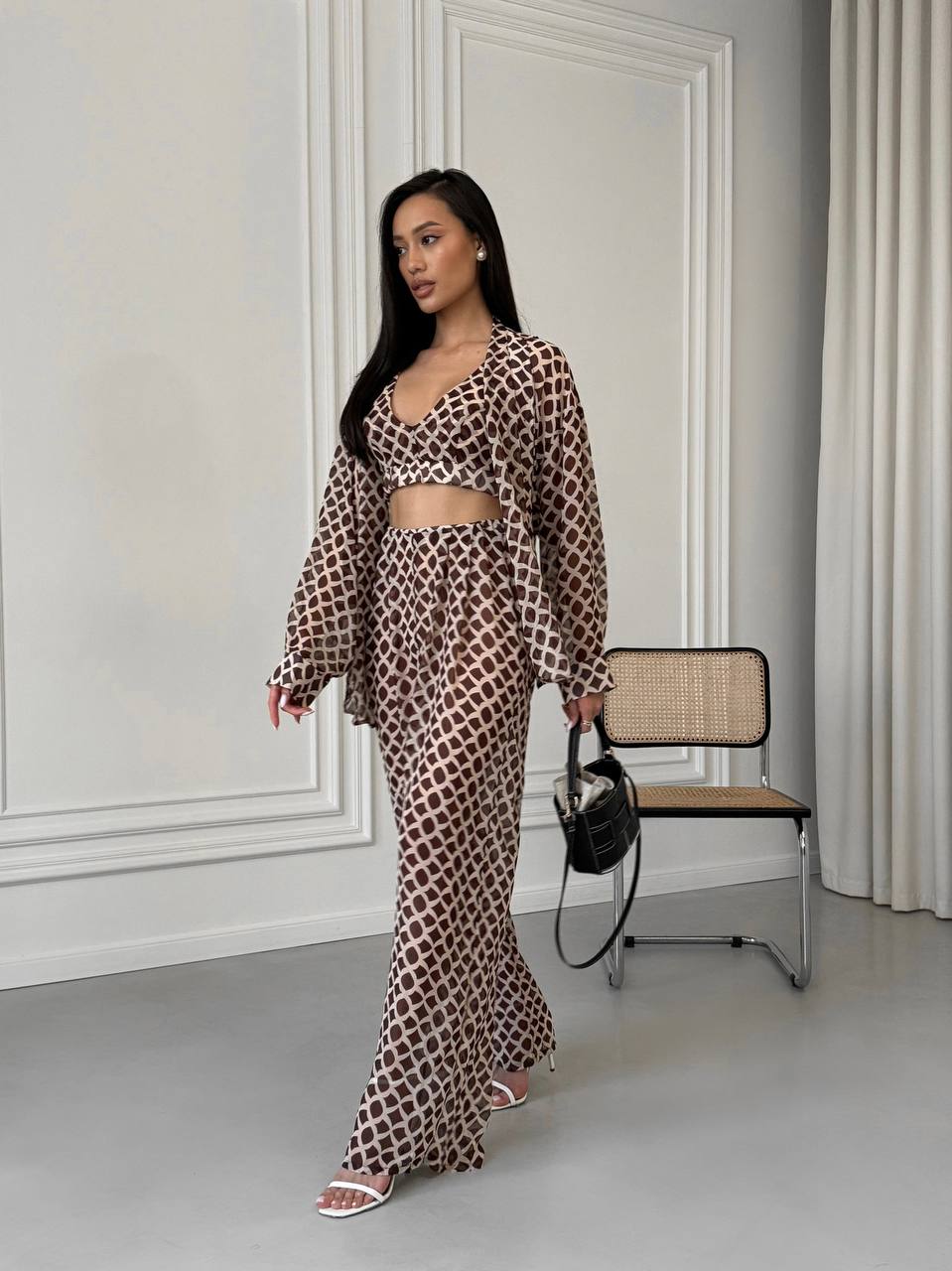 Woman in a leopard print outfit standing in a room with a chair and wall.