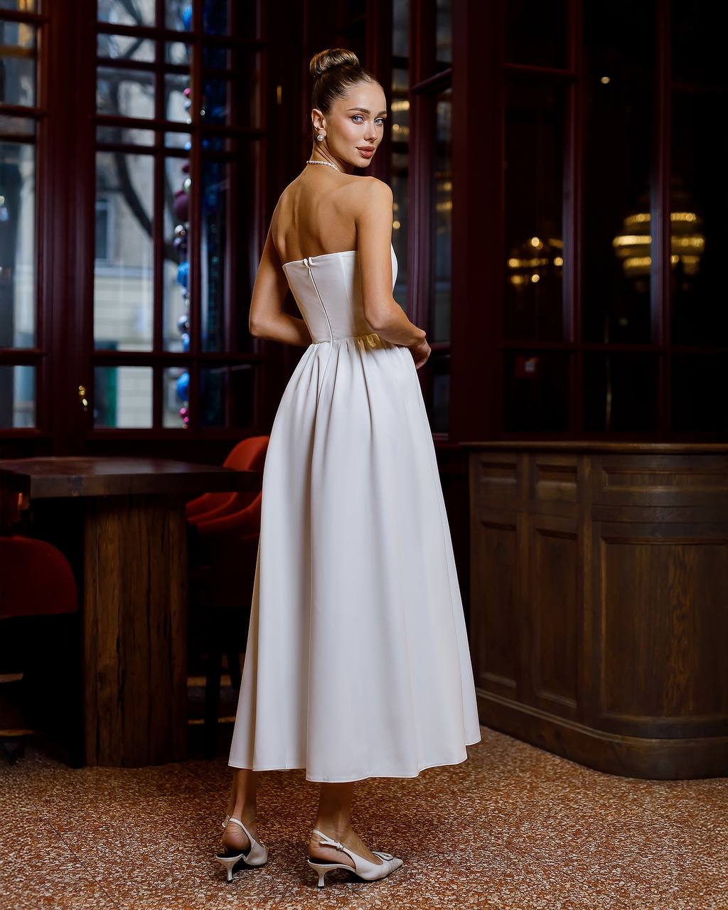 Woman in a white strapless dress standing in an elegant interior setting.