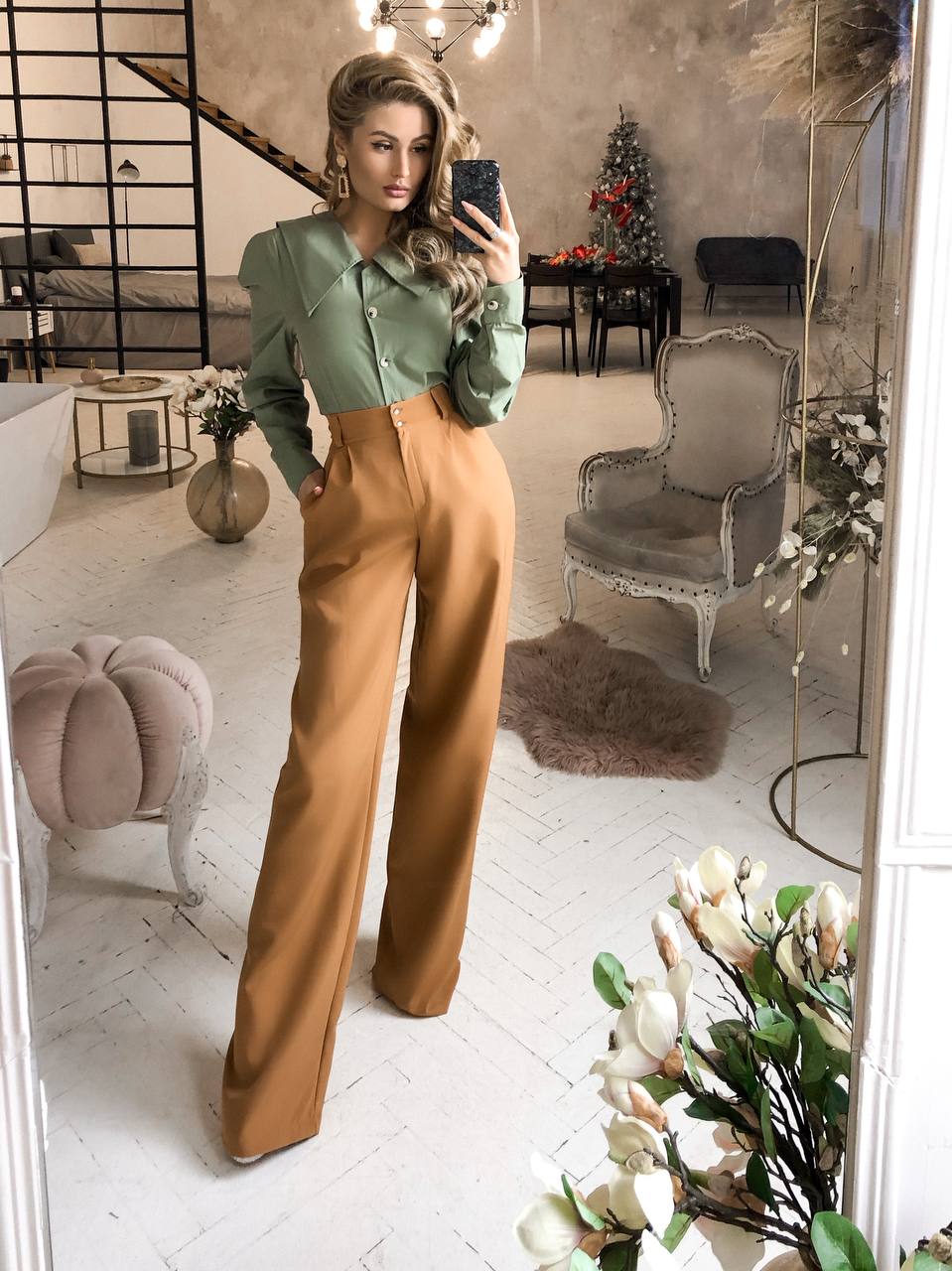 Woman taking a mirror selfie in a stylish outfit with a modern interior setting.
