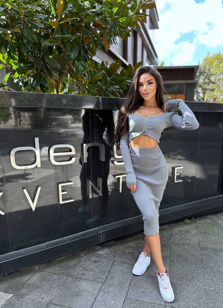 Woman in a gray outfit standing in front of a building with a sign.