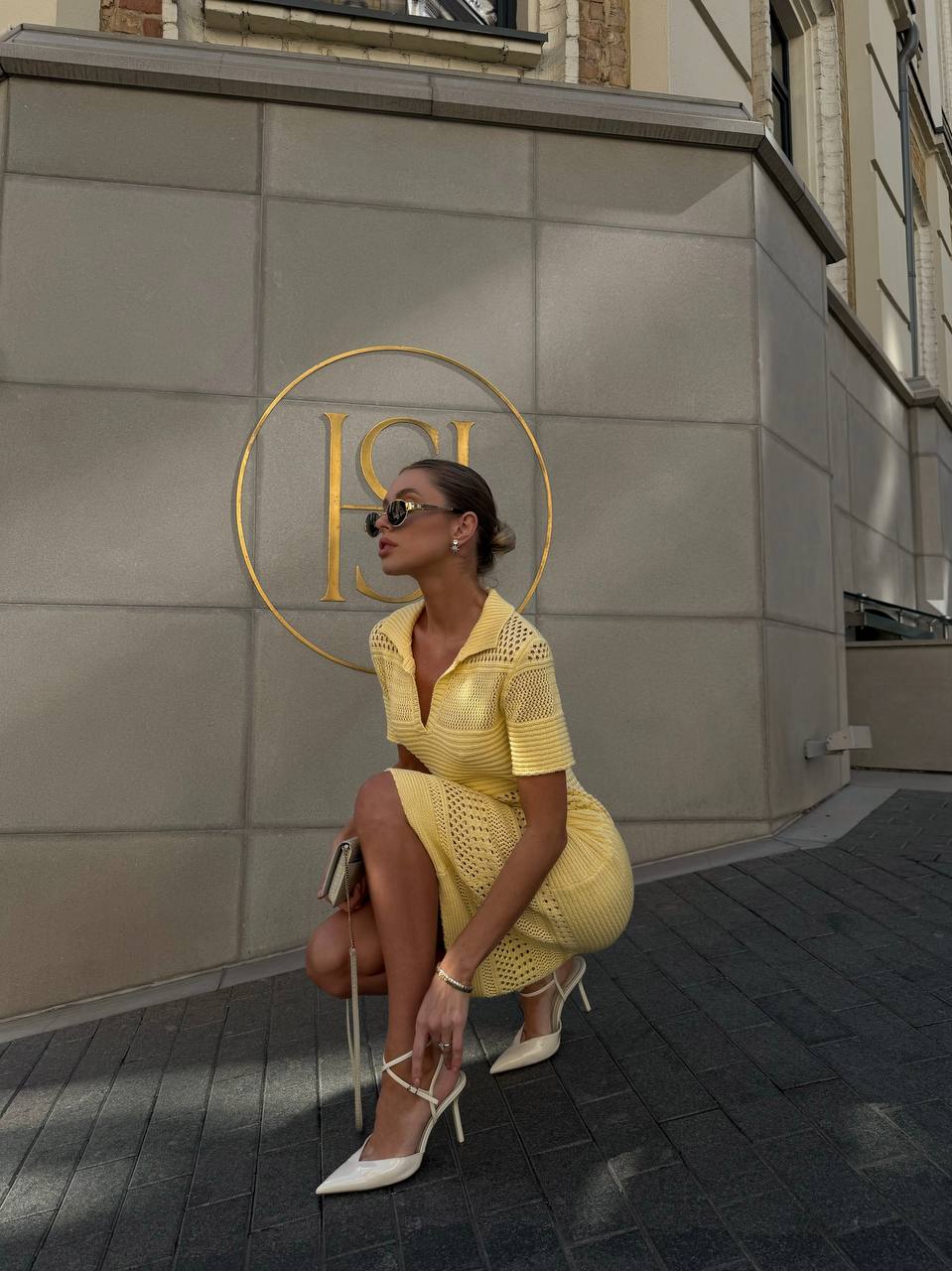 Woman in a yellow dress sitting on a chair in front of a building with a gold logo.