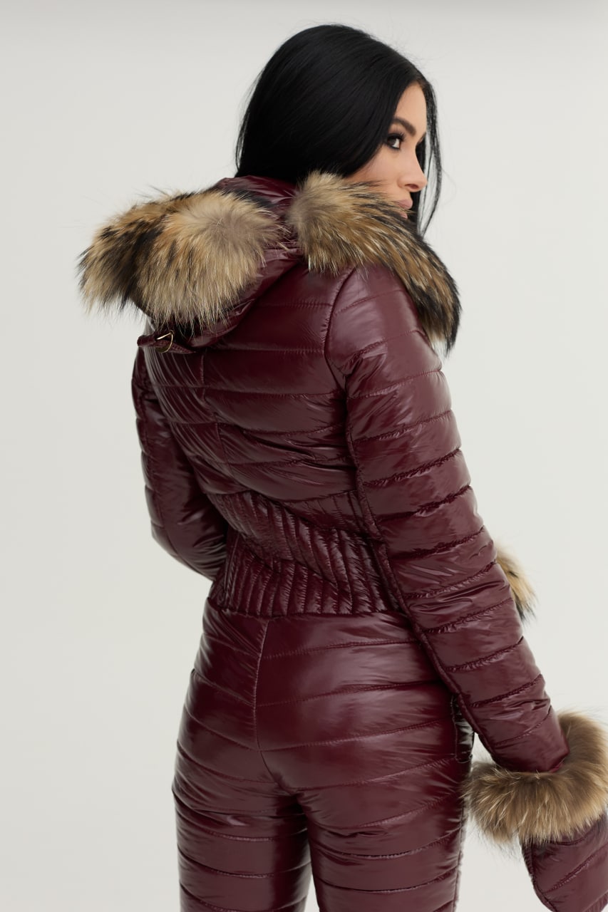 Person wearing a maroon puffer jacket with fur trim on a white background