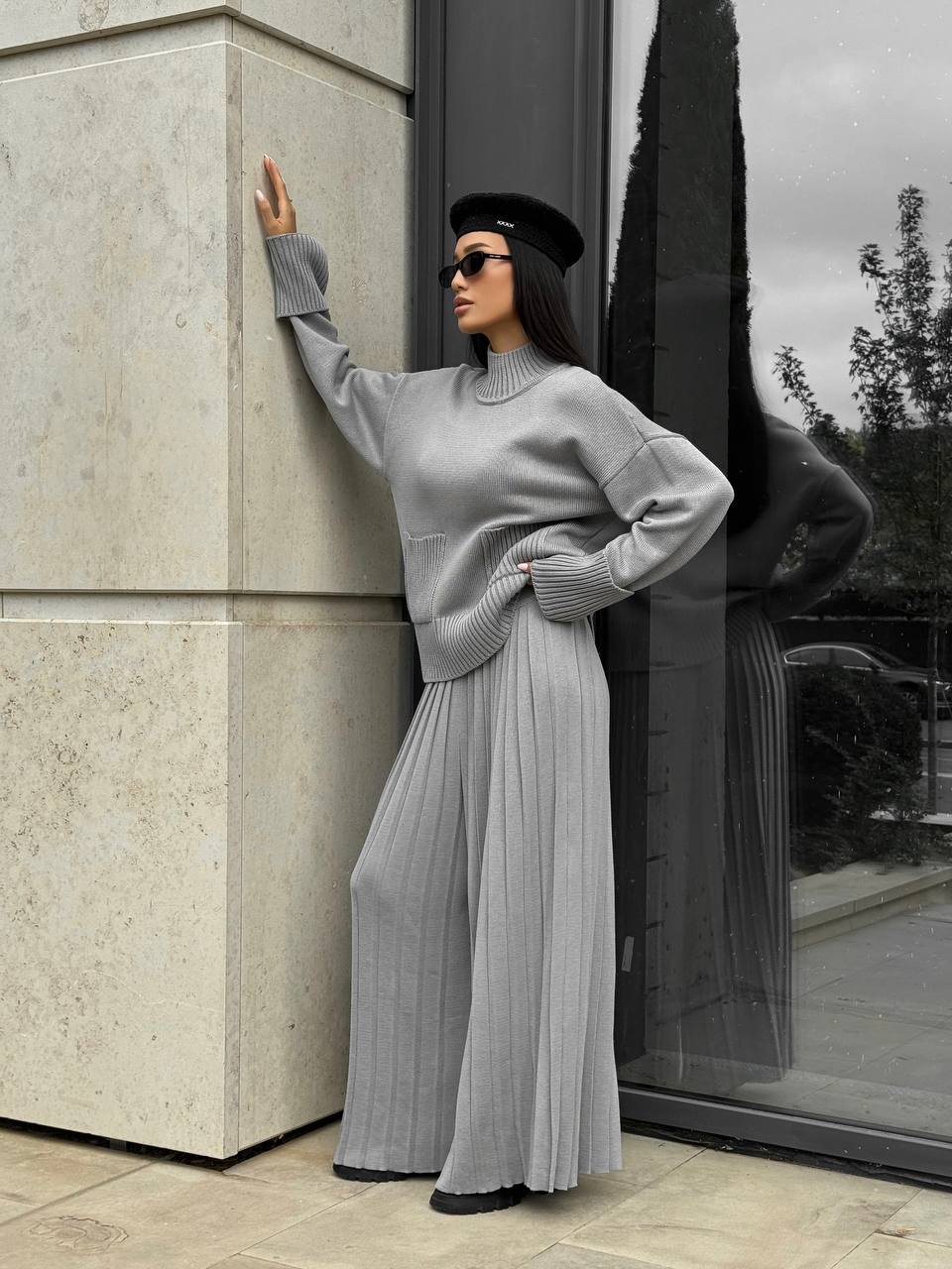 Woman in a gray outfit standing against a building