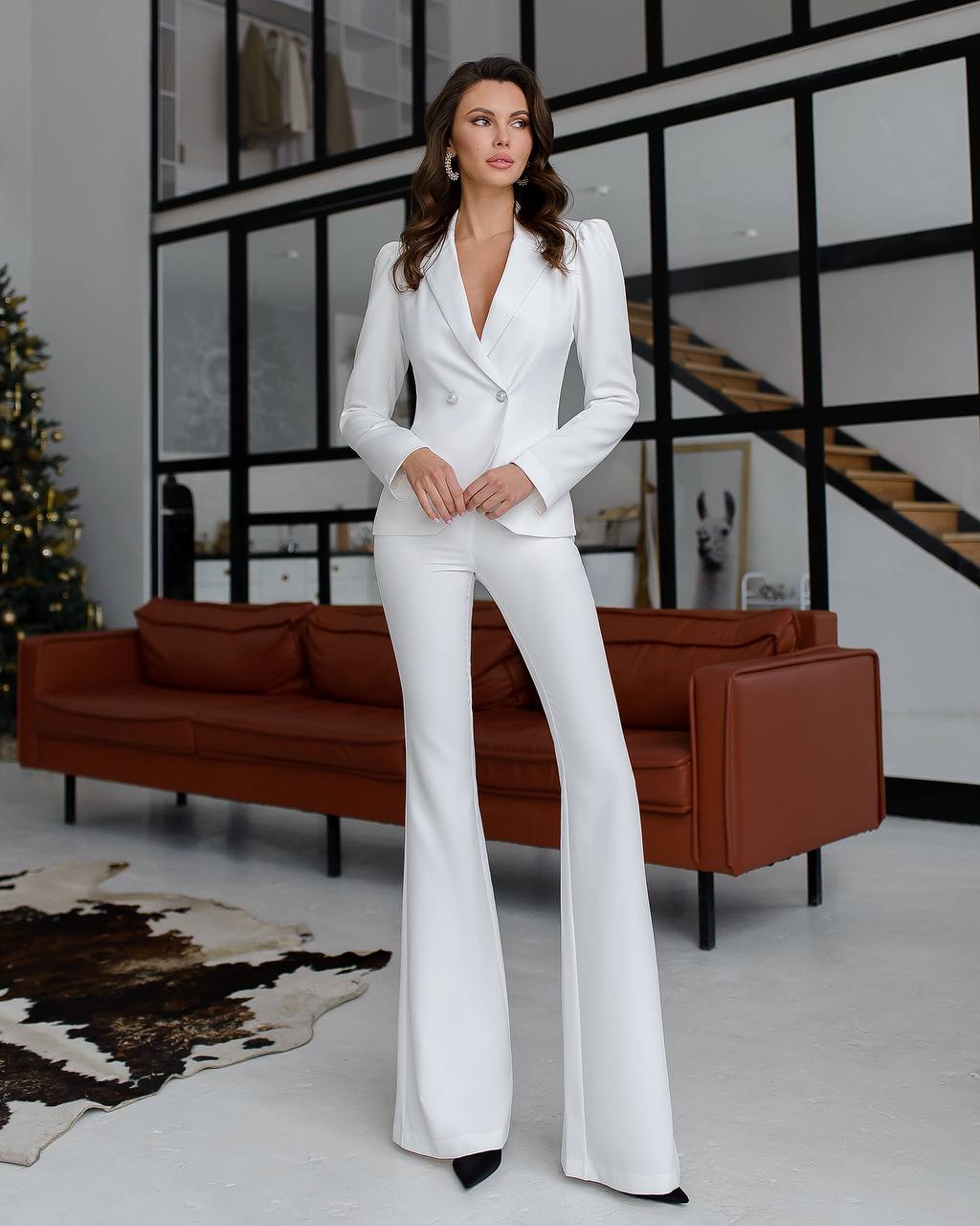 Woman in a white suit standing in a modern living room.