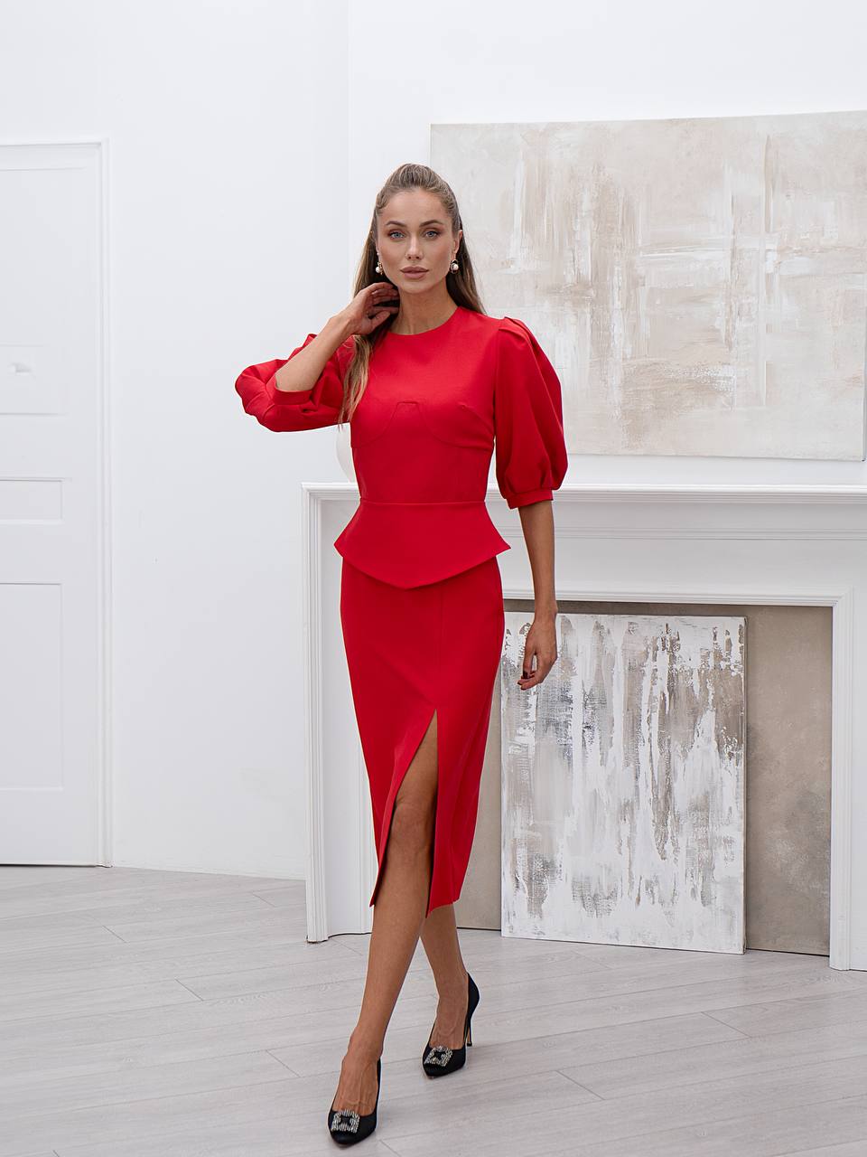 Woman wearing a red dress with puff sleeves in a minimalistic room.
