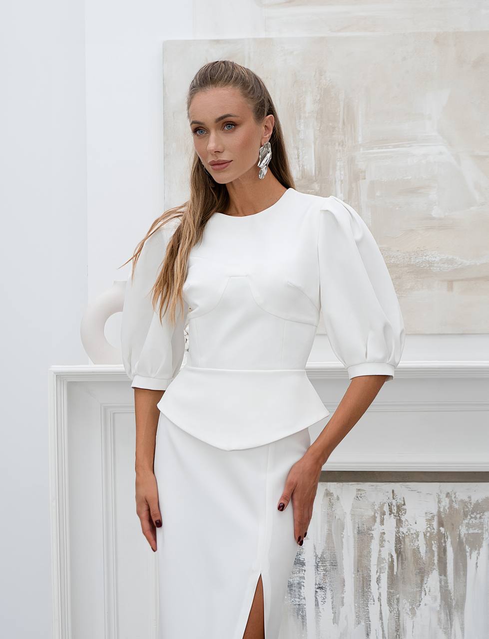 Woman wearing a white outfit with puffed sleeves against a light background