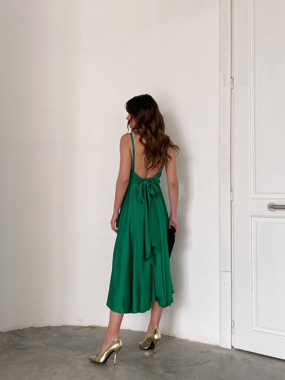 Woman in a green dress standing against a white wall.