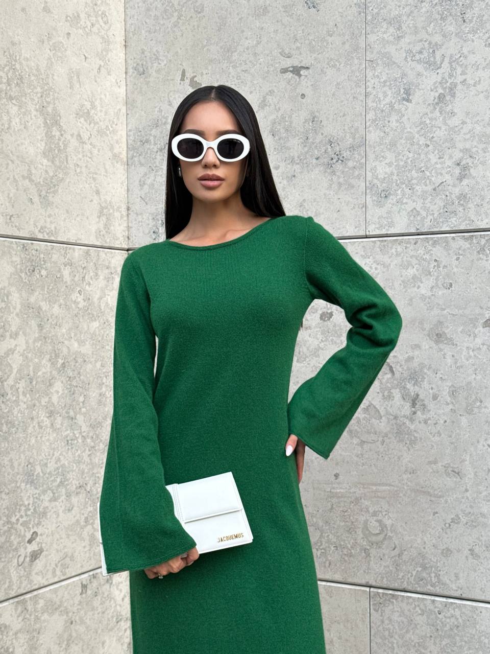 Woman in a green dress holding a white clutch against a gray wall