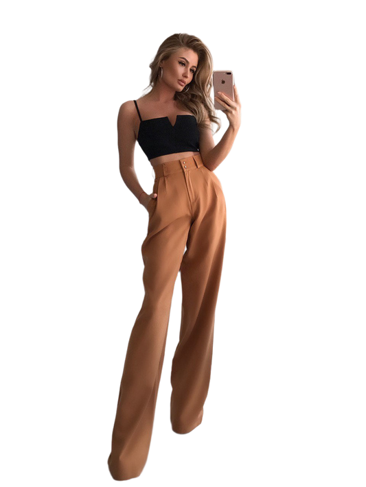 Woman taking a selfie wearing a black top and tan high-waisted pants on a white background