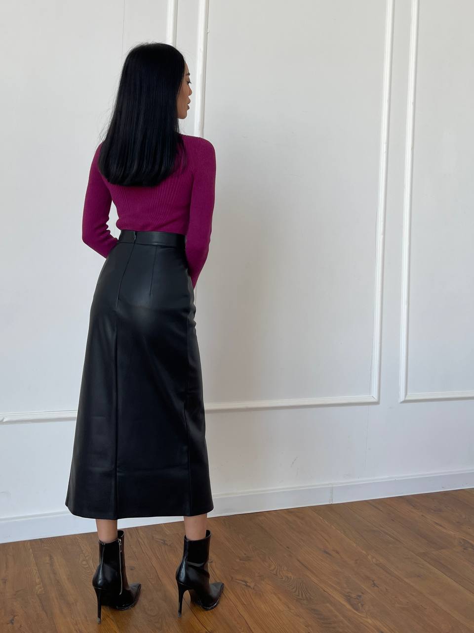 Person wearing a black leather skirt and purple top in a minimal indoor setting