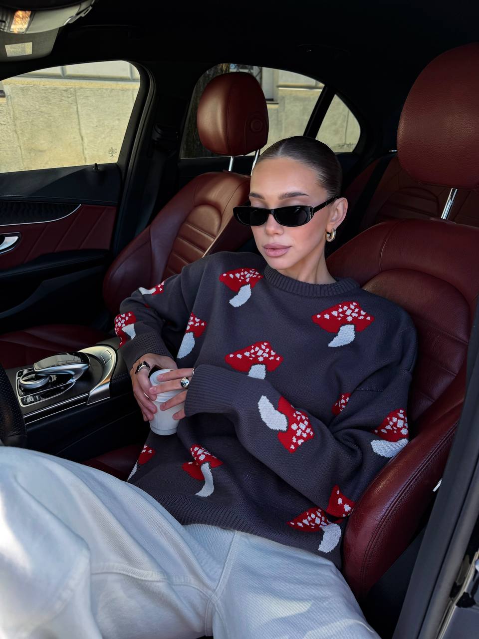 Person sitting in a car wearing a dark sweater with red and white patterns
