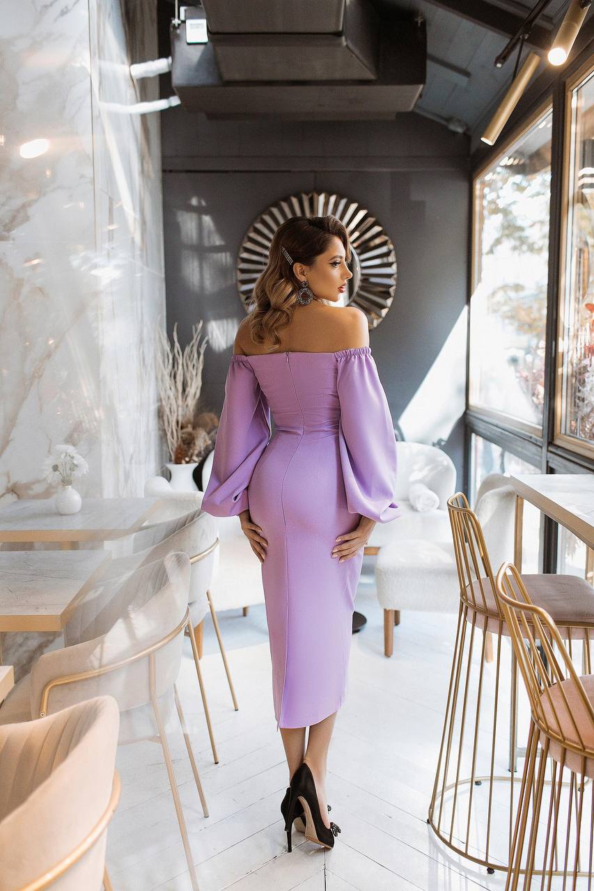 Woman in a purple off-shoulder dress standing in a modern interior setting.