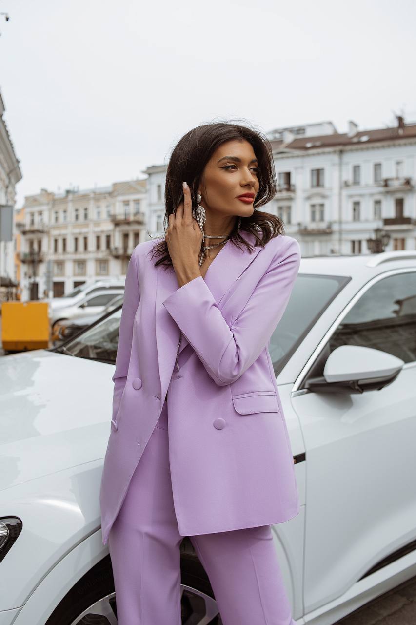 Woman in a lavender suit standing next to a white car with a cityscape background
