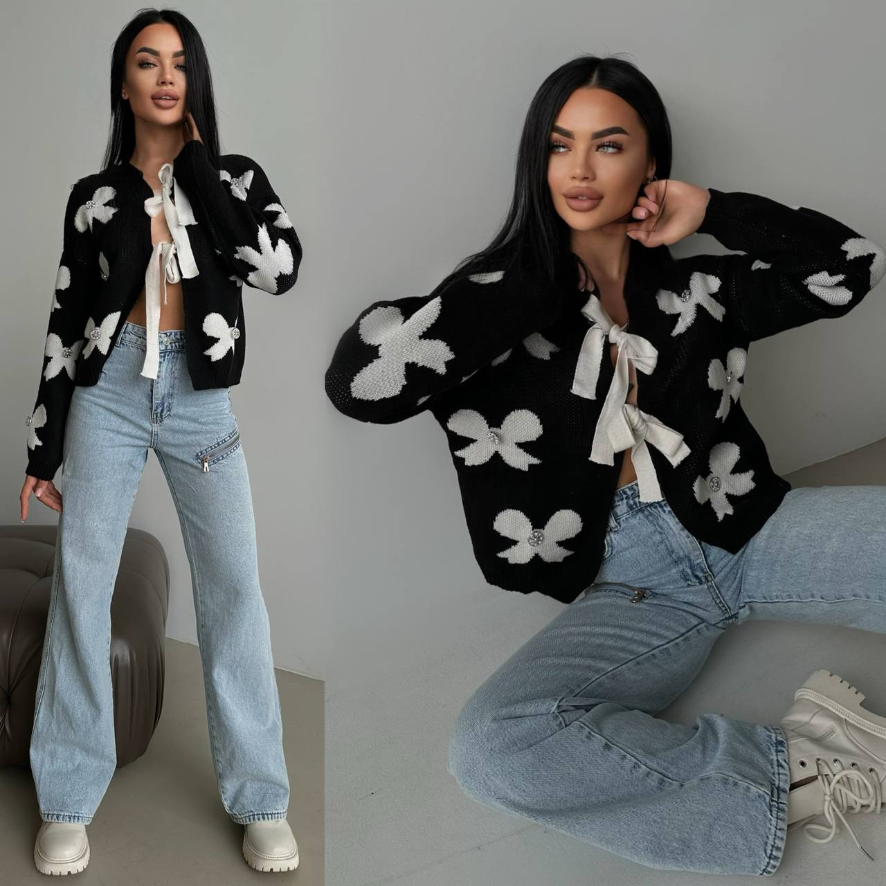 Woman wearing a black cardigan with white floral patterns and blue jeans, sitting on a chair.