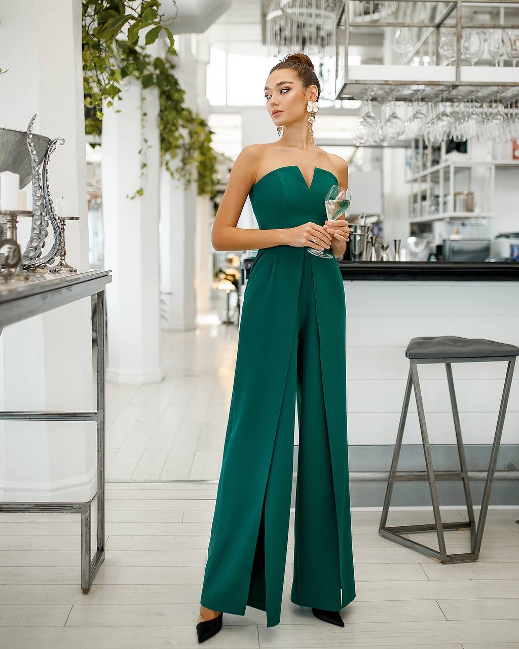 Woman in a green strapless jumpsuit standing in a modern kitchen.