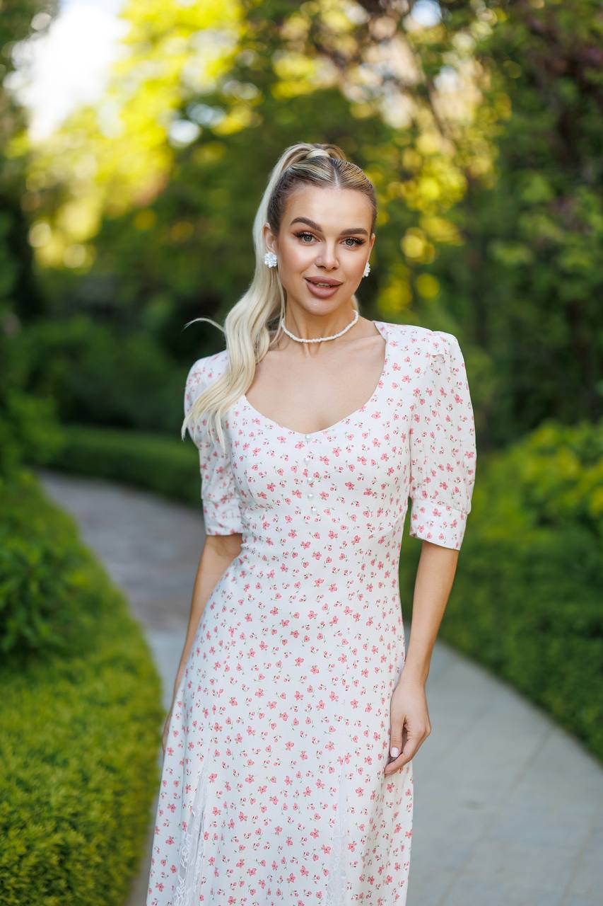Woman in a floral dress standing outdoors with greenery in the background