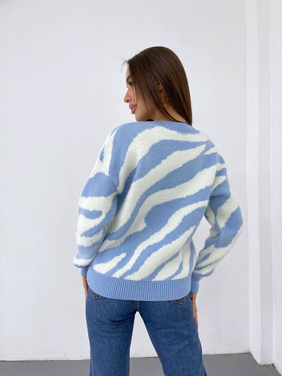 Woman wearing a blue and white patterned sweater against a white wall.
