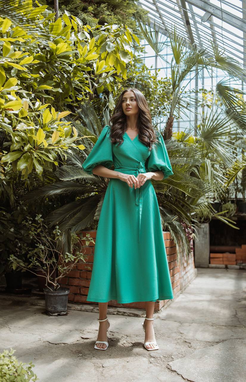 Woman in a teal dress standing in a greenhouse filled with plants