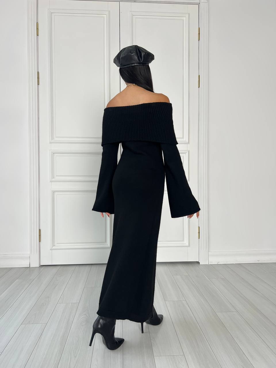 Person wearing a black off-shoulder top and wide-leg pants in a minimalistic room.