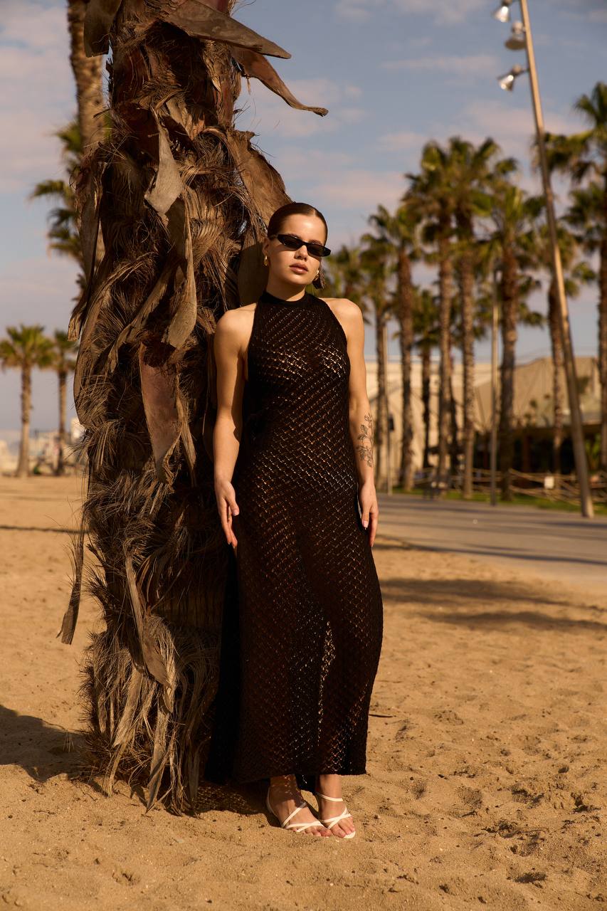 Woman in a black dress standing on a sandy beach with palm trees in the background