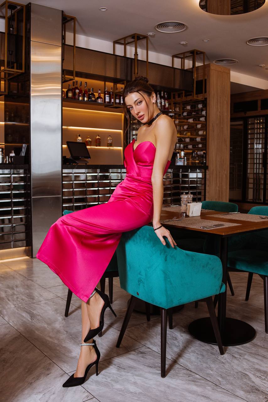 Woman in a pink dress sitting on a teal chair in a restaurant setting.