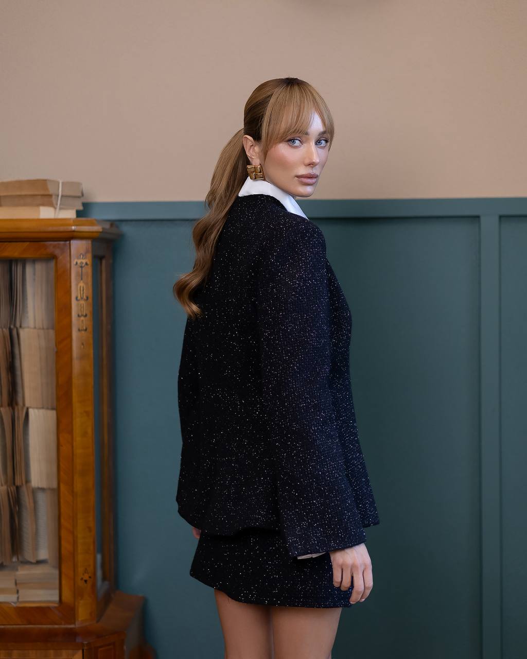 Woman wearing a dark blazer and skirt set in a room with a bookshelf.